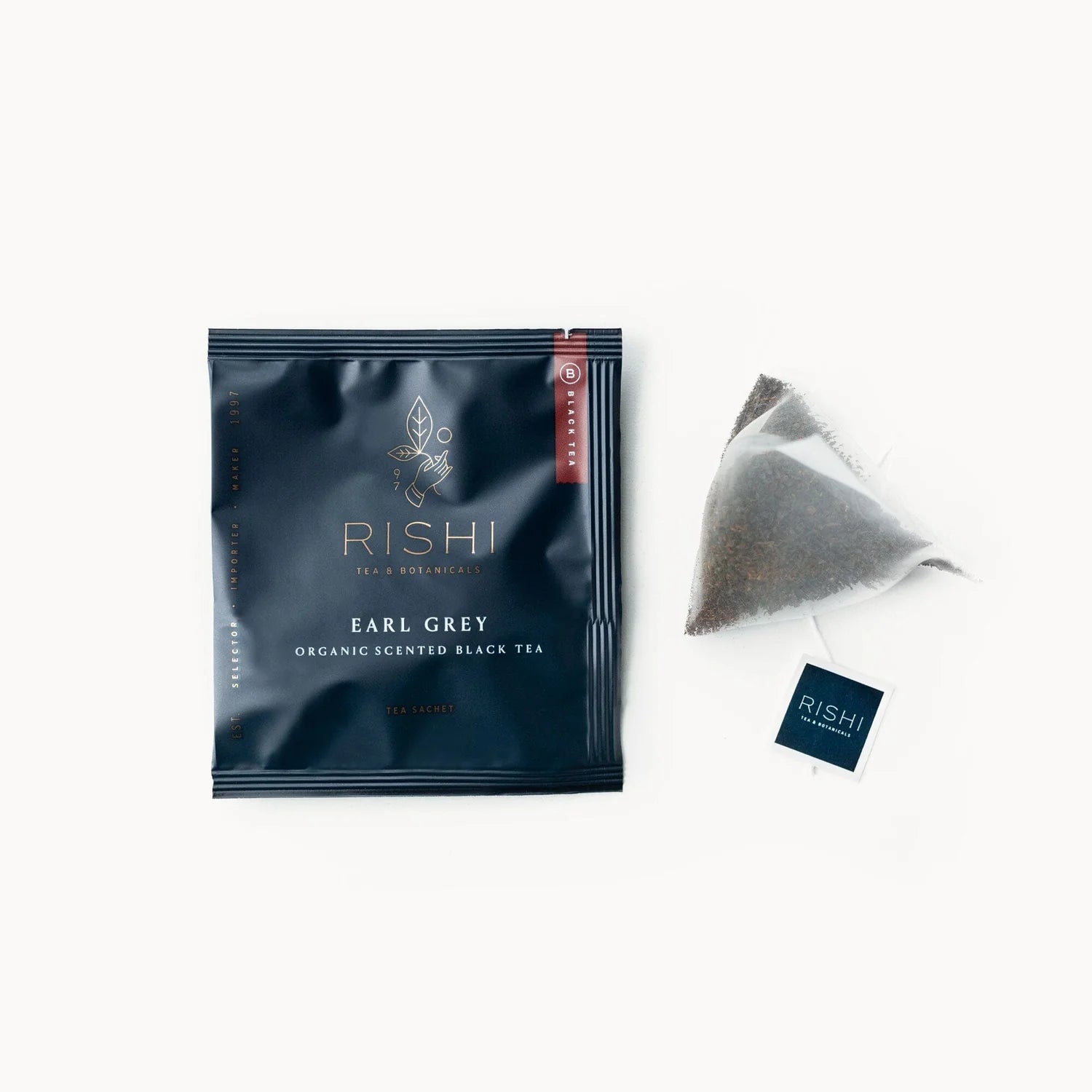 A tea sachet package with the brand name RISHI and the product name Earl Grey Organic Ceylon Black Tea displayed, alongside an individual tea sachet and a business card.