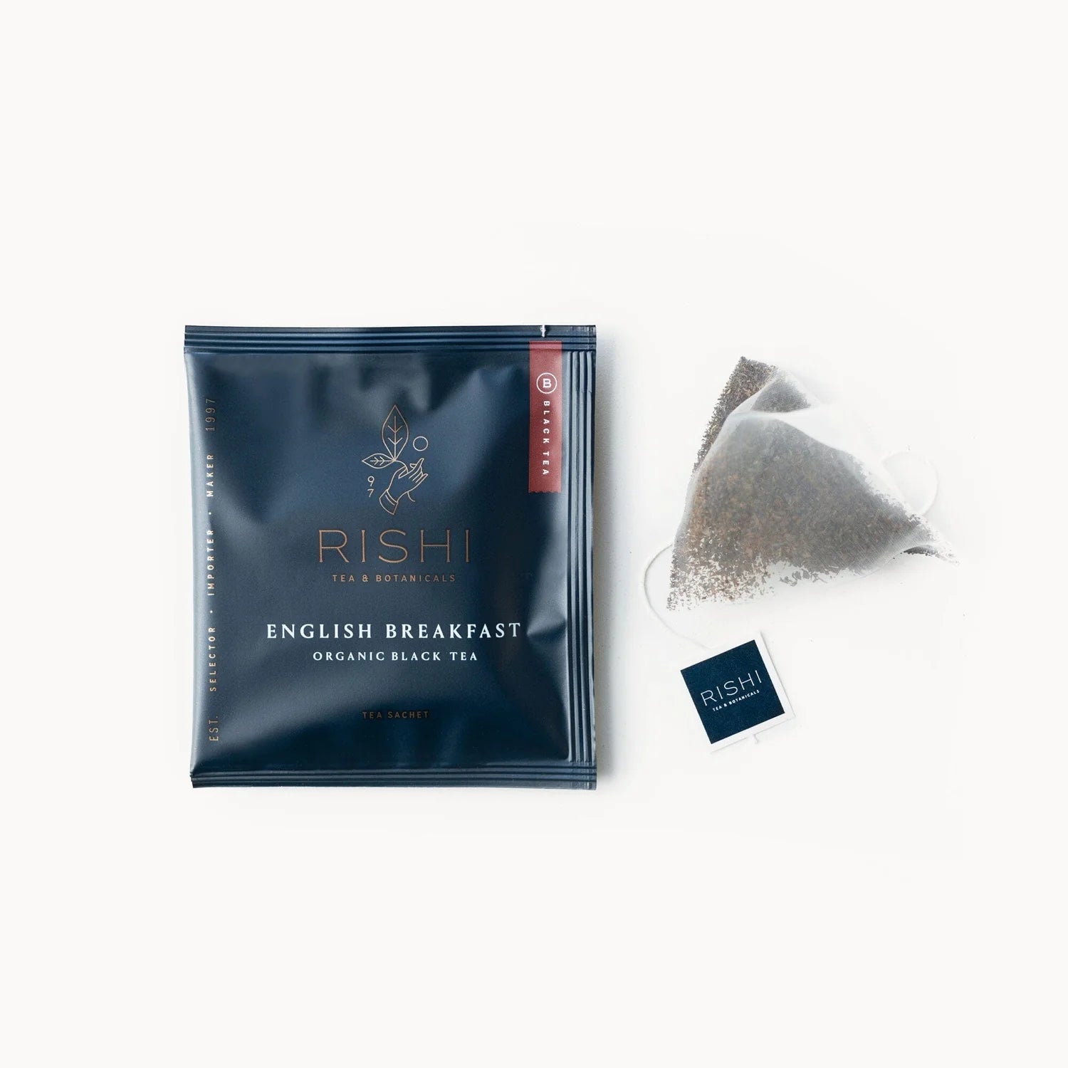 A packaged English breakfast tea sachet with the brand RISHI visible, alongside an unfolded tea bag showing the loose leaf inside.